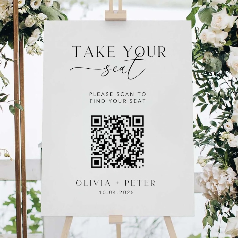 May include: A white wedding sign with the text "TAKE YOUR seat" and "PLEASE SCAN TO FIND YOUR SEAT". A QR code is below the text, followed by "OLIVIA + PETER" and the date "10.04.2025". The sign is on an easel.