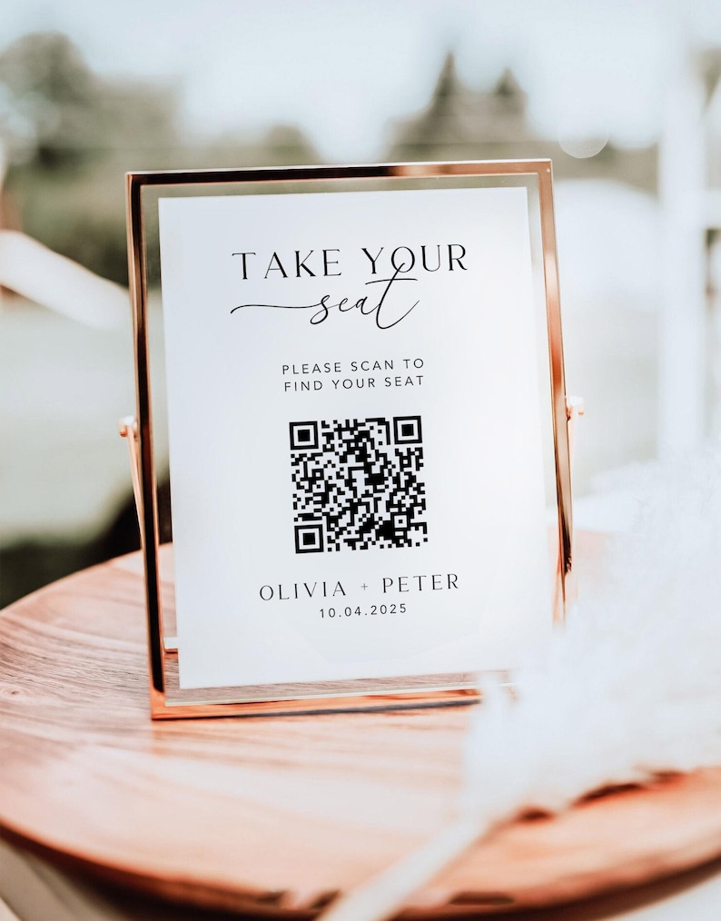 May include: A gold-framed sign with the text "TAKE YOUR seat" and a QR code. Below the QR code are the names "OLIVIA + PETER" and the date "10.04.2025". The sign is displayed on a wooden surface, likely for a wedding or event.