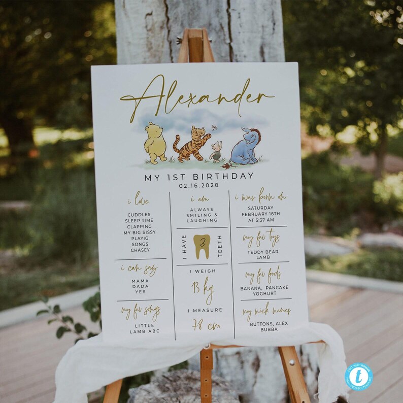 K&ouml;nnte beinhalten: Ein wei&szlig;es und goldenes Schild zum ersten Geburtstag mit den Figuren Winnie Puuh, Tigger und Esel. Das Schild zeigt den Namen des Kindes, Alexander, und Details zu seinem ersten Jahr, einschlie&szlig;lich seines Gewichts, seiner Gr&ouml;&szlig;e und seiner Lieblingsessen.