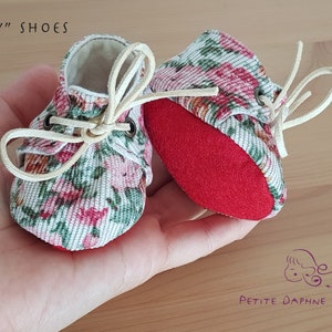May include: A pair of miniature floral print shoes with red soles and white laces. The shoes are tied with a bow and the text "ROSY" SHOES is visible in the image.