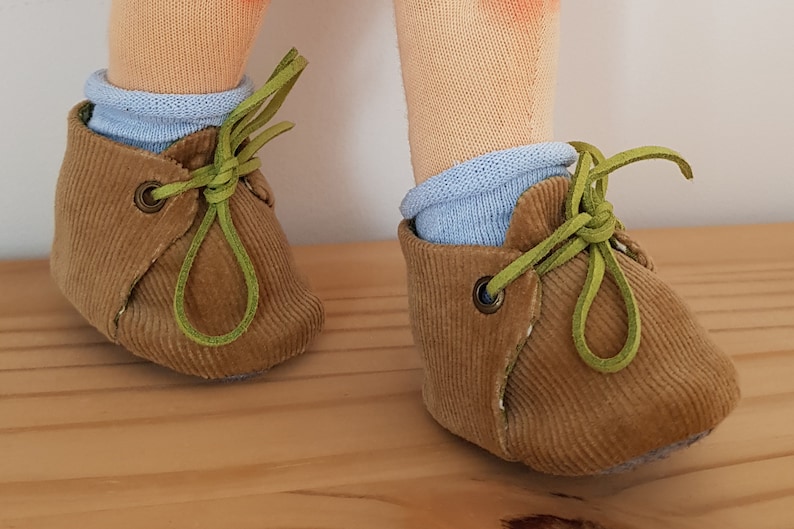 May include: A pair of brown corduroy baby shoes with green laces. The shoes have a light blue sock inside.