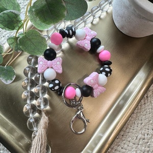 May include: A pink and black polka dot beaded keychain with a pink bow charm and a silver key ring.