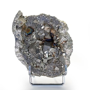 May include: A raw pyrite specimen, a metallic mineral with a crystalline structure. The pyrite is a dark gray color with shiny, reflective surfaces. The specimen is displayed on a chrome stand against a white background.