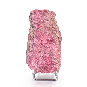 Puede incluir: Un espécimen de piedra preciosa de rodocrosita rosa en bruto. El mineral tiene una textura en capas y está montado en un pequeño soporte metálico plateado. La piedra muestra diferentes tonos de rosa y un aspecto natural sin pulir.