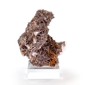 May include: A mineral specimen featuring a cluster of dark brown, needle-like crystals. The crystals are densely packed, creating a textured appearance. The mineral sits on a clear, rectangular acrylic base, showcasing its natural form.