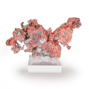 Peut inclure: Un spécimen de cuivre naturel à la forme complexe et irrégulière, présentant un mélange de teintes brun-rouge et gris-vert. Le cuivre est monté sur un socle en acrylique transparent avec une base blanche, mettant en valeur sa texture et sa forme uniques.