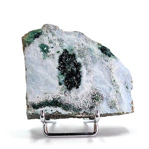 Può includere: Un campione minerale con una superficie azzurra e bianca con formazioni cristalline verde scuro. La roccia è esposta su un supporto in metallo argentato, che mette in risalto le sue trame e colori naturali. Il tema è la geologia e i minerali naturali.