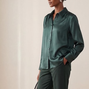 Puede incluir: Una camisa de satén verde oscuro y pantalones a juego. El conjunto se combina con bailarinas negras y un gran bolso tote negro. El conjunto es monocromático y elegante.
