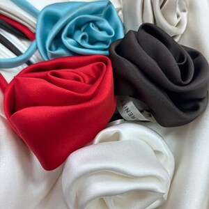 May include: Five silk rose hair ties in different colors: white, light blue, red, black, and cream. The hair ties are arranged in a circle on a white background.