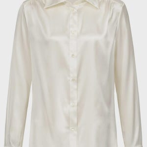 Puede incluir: Una camisa de manga larga con botones en un lustroso color crema blanquecino. La camisa presenta un cuello cl&aacute;sico en punta, una tapeta frontal con botones a juego y pu&ntilde;os estructurados en las mu&ntilde;ecas. La tela tiene un acabado suave y satinado.