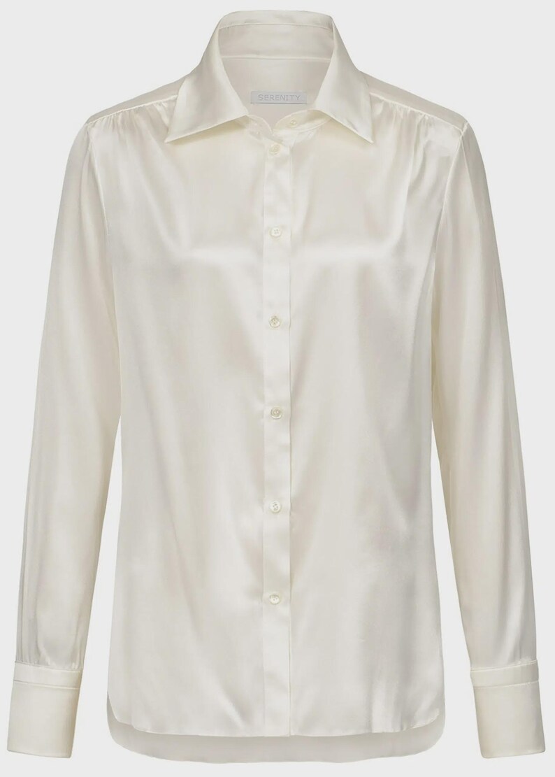 Puede incluir: Una camisa de manga larga con botones en un lustroso color crema blanquecino. La camisa presenta un cuello cl&aacute;sico en punta, una tapeta frontal con botones a juego y pu&ntilde;os estructurados en las mu&ntilde;ecas. La tela tiene un acabado suave y satinado.