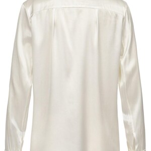 Puede incluir: Una camisa de manga larga con botones en un color blanco roto s&oacute;lido con un acabado suave y brillante. La camisa presenta un cuello cl&aacute;sico, un canes&uacute; en la espalda y pu&ntilde;os con dos botones en cada manga, vista desde la parte posterior.