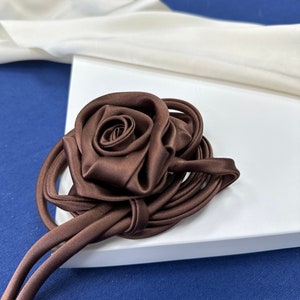 May include: A brown satin rose with a long brown satin ribbon. The rose is tied in a knot and the ribbon is loose.