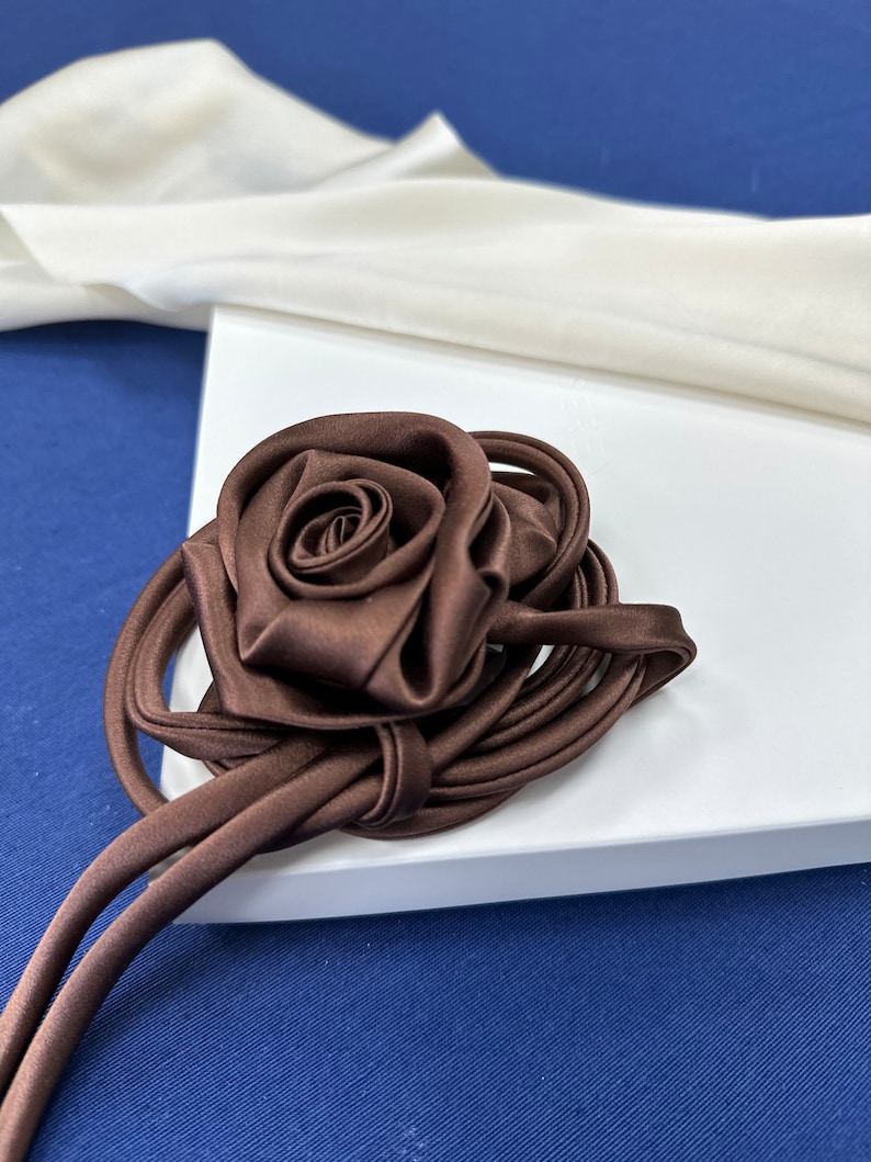 May include: A brown satin rose with a long brown satin ribbon. The rose is tied in a knot and the ribbon is loose.