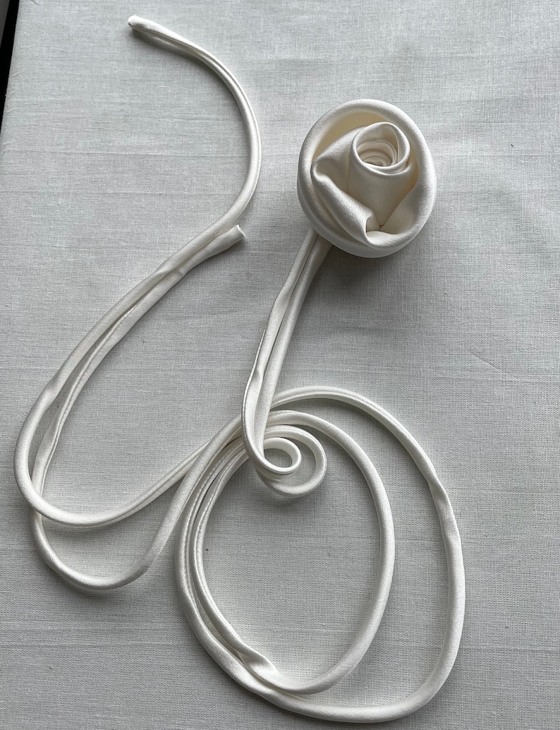 May include: A white satin ribbon tied into a rose shape with the ends of the ribbon forming a loose circle.