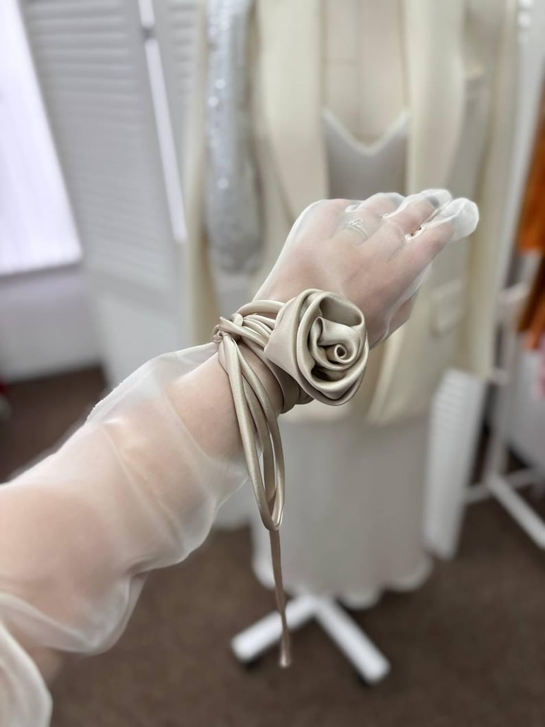 May include: A sheer white glove with a satin rose tied around the wrist.