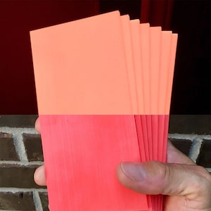 May include: A stack of eight bright orange and red rectangular cards. The cards are held in a hand.