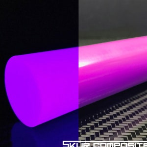 Könnte beinhalten: Eine Rolle leuchtend pinkfarbener Vinylfolie, die unter Schwarzlicht in einem leuchtenden Lila leuchtet. Die Folie wird auf einem schwarzen Carbonfaser-Hintergrund gezeigt.
