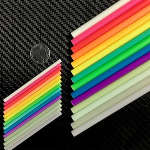 Może przedstawiać: Zestaw 18 świecących w ciemności pręt&oacute;w w r&oacute;żnych kolorach, w tym białym, r&oacute;żowym, pomarańczowym, ż&oacute;łtym, zielonym, niebieskim, fioletowym i szarym. Pręty są ułożone w kształcie tęczy.