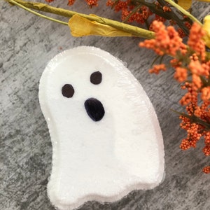 Może przedstawiać: Biała bomba do kąpieli w kształcie ducha z czarnymi oczami i ustami. Bomba do kąpieli jest owinięta w przezroczysty plastik. Pomarańczowe jagody i ż&oacute;łte liście w tle.