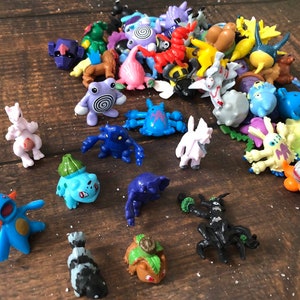 Może przedstawiać: Kolekcja kolorowych plastikowych figurek Pokemon&oacute;w, w tym Pikachu, Bulbasaur, Charmander, Squirtle i wiele innych. Figurki są ułożone na drewnianej powierzchni.