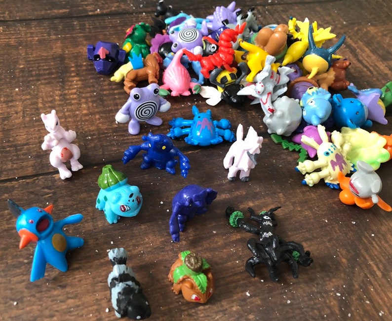 Może przedstawiać: Kolekcja kolorowych plastikowych figurek Pokemon&oacute;w, w tym Pikachu, Bulbasaur, Charmander, Squirtle i wiele innych. Figurki są ułożone na drewnianej powierzchni.