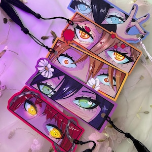 Puede incluir: Colección de marcapáginas de estilo anime con ilustraciones detalladas de ojos. Cada marcapáginas tiene un diseño único con colores vibrantes, incluyendo azul, naranja, verde y rojo. Borlas negras están unidas a cada marcapáginas.