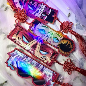 May include: Three rectangular bookmarks featuring holographic anime-style character illustrations with vibrant colors. Each bookmark is accented with a decorative red knotted cord and a long red tassel, showcasing detailed eye and hand motifs.