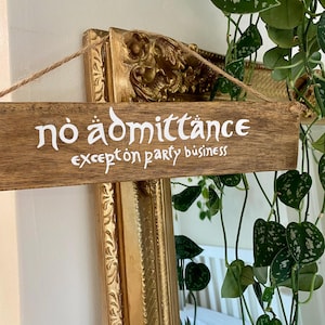 May include: A rectangular wooden sign with a natural brown grain finish, suspended by a thin jute twine. The sign features white lettering that reads "no admittance except on party business" in a stylised, fantasy-inspired font.