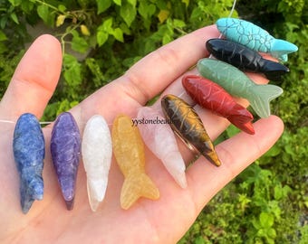May include: A collection of gemstone fish carvings in various colors, including blue, purple, white, yellow, pink, red, green, black, and tiger's eye. The fish are strung together on a thin, clear thread. The text "yystonebeads" is visible.