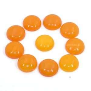 May include: Ten round, orange cabochon gemstones arranged in a circle on a white background.