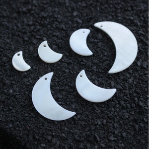 Könnte beinhalten: Sechs weiße, halbmondförmige Muschelanhänger in verschiedenen Größen. Die Anhänger haben oben ein Loch zum Aufziehen.