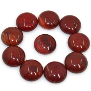 Könnte beinhalten: Zehn runde, glatte, rote Jaspis-Cabochons mit polierter Oberfläche. Die Cabochons sind in einem Kreis auf weißem Hintergrund angeordnet.