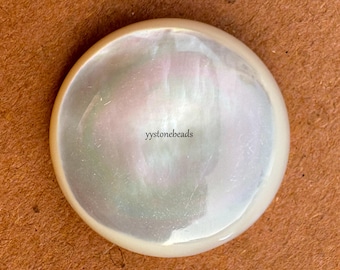 May include: A circular, smooth, iridescent mother-of-pearl button with a glossy finish. The surface displays subtle swirls of white, cream, and soft pink tones. The text 'yystonebeads' is printed in black in the centre of the button.