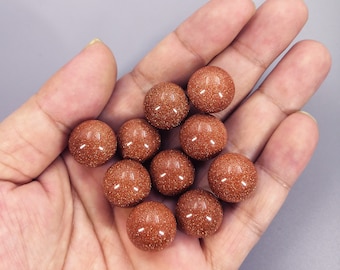 May include: A collection of 12 smooth, round, red-brown sandstone beads. The beads are arranged in a pyramid shape in a hand.