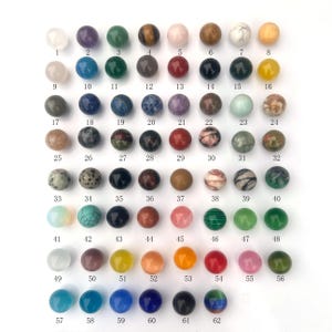 May include: A grid of 62 small, round, polished stones in various colors and patterns. Each stone is numbered from 1 to 62.