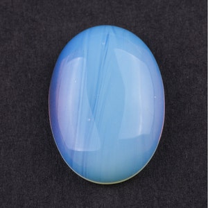 Peut inclure: Une pierre précieuse ovale de couleur bleu clair en forme de cabochon avec des tourbillons blancs et bleu clair. La pierre précieuse a une surface lisse et polie.