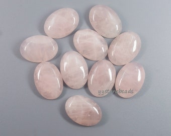 May include: Ten oval-shaped rose quartz cabochons, each with a smooth, polished surface and a pale pink color. The stones are arranged in a loose cluster on a gray background.