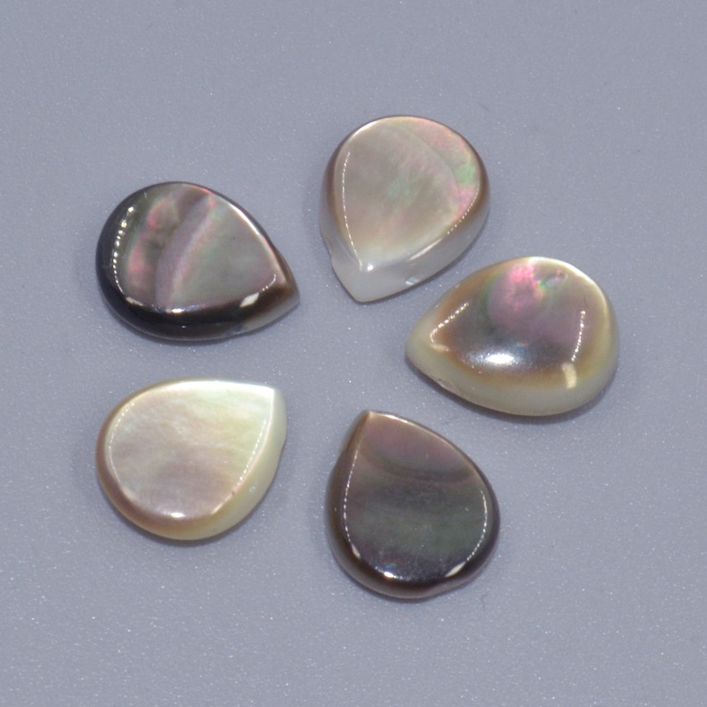 May include: Five iridescent mother of pearl teardrop shaped cabochons. The cabochons are various shades of grey, black, and white.