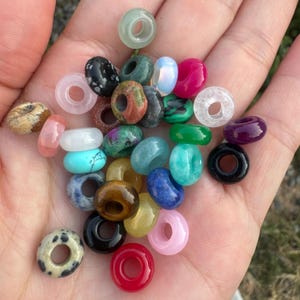 Op de afbeelding: Een verzameling kleurrijke edelsteen donut kralen, elk met een gat in het midden. De kralen zijn gemaakt van verschillende natuurlijke stenen, waaronder amethist, turquoise en agaat.