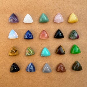 Może przedstawiać: Dwudzieścia cztery trójkątne kaboszony z kamieni szlachetnych w różnych kolorach i wzorach, w tym ametyst, biały, zielony, różowy kwarc, żółty, opal, lapis lazuli, różowy, czarny, zielony, tygrysie oko, turkusowy i inne.