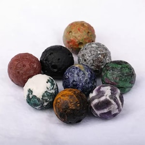 May include: A collection of ten spherical decorative objects in various colors and textures. The spheres include shades of red, black, white, blue, green, and brown, with a variety of patterns and surface details. The objects appear to be made of stone or a similar material.