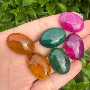 May include: Six agate cabochons in various colors, including green, orange, pink, and brown. The cabochons are smooth and polished, with a natural, organic pattern.