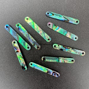 Puede incluir: Surtido de formas rectangulares de concha de abulón iridiscente con agujeros en cada extremo. Son perfectas para la elaboración de joyas o manualidades.