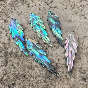 May include: Five iridescent abalone shell feather pendants. The feathers display a range of colors, including blues, greens, and purples, with a pearlescent sheen. Each feather has a small hole at the top for stringing.