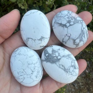 May include: Four white howlite tumbled stones with gray veining. The stones are smooth and oval shaped.