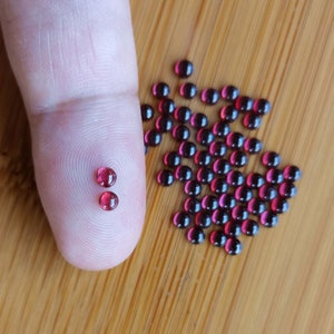 Peut inclure: Gros plan sur deux petites perles de verre rondes rouges à côté d'un tas plus grand de perles similaires. Les perles sont toutes à peu près de la même taille et de la même forme, et elles sont toutes d'une couleur rouge foncé.
