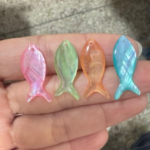 Puede incluir: Cuatro abalorios en forma de pez iridiscentes en rosa, verde, naranja y azul. Los abalorios tienen un acabado nacarado y son perfectos para la elaboración de joyas.