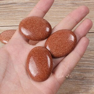 May include: Four smooth, oval-shaped stones with a reddish-brown color and a speckled texture. The stones are held in a hand.