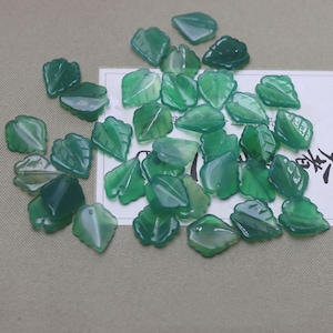 Puede incluir: Un montón de cuentas de jade verde en forma de hoja. Las cuentas están talladas en jade verde y tienen un acabado liso y pulido.